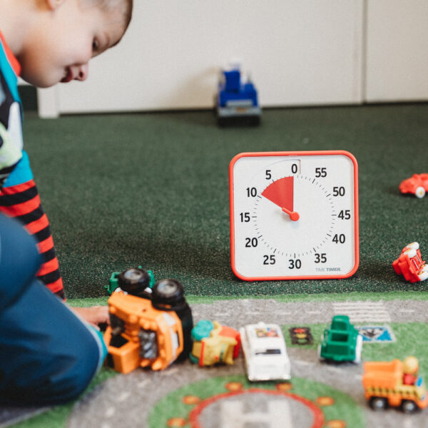 Ett barn leker med bilar och en orange Time Timer Medium klocka står bredvid