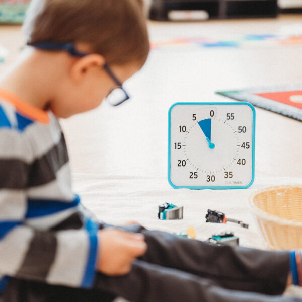 Ett barn leker på golvet och en blå Time Timer Medium klocka står bredvid.